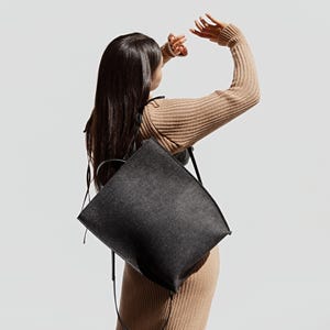 May include: A person wearing a brown sweater and a black felt backpack with a black leather strap.