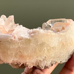 Könnte beinhalten: Ein Cluster aus rosa und weißen Quarzkristallen mit einer klaren Quarzspitze oben. Die Kristalle sind in einer natürlichen Formation angeordnet und haben eine raue, strukturierte Oberfläche.