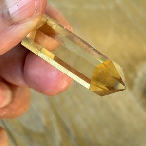 Könnte beinhalten: Eine klare, gelbe Kristallspitze mit einer spitzen Spitze. Der Kristall ist glatt und poliert.