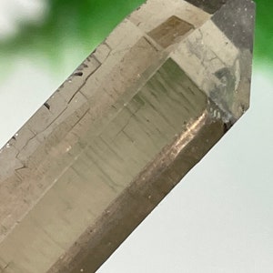 Può includere: Una punta di cristallo di quarzo trasparente con una tonalità marrone fumè. Il cristallo ha una finitura naturale e grezza e misura circa 5 cm di lunghezza.