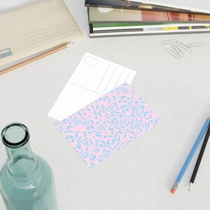May include: A pink postcard with a blue and white pattern of Greek letters and a leopard print design. The postcard is blank on the back.