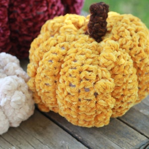 May include: A crocheted pumpkin with a brown stem. The pumpkin is made of yellow yarn with a velvety texture.