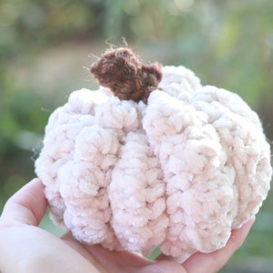 May include: A crocheted pumpkin with a brown stem. The pumpkin is made of a soft, fluffy yarn and is a light pink color.