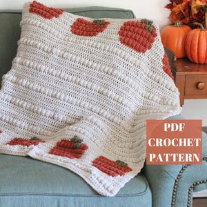 May include: Cream-colored crocheted blanket with textured stitchwork and repeating pumpkin motifs in shades of orange and green. The blanket is draped over a teal armchair. The text "PDF CROCHET PATTERN" is visible.
