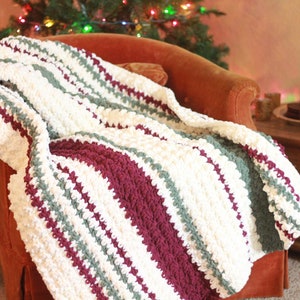 May include: A white, green, and burgundy striped crocheted throw blanket draped over a red armchair. The blanket has a textured, puffy look.