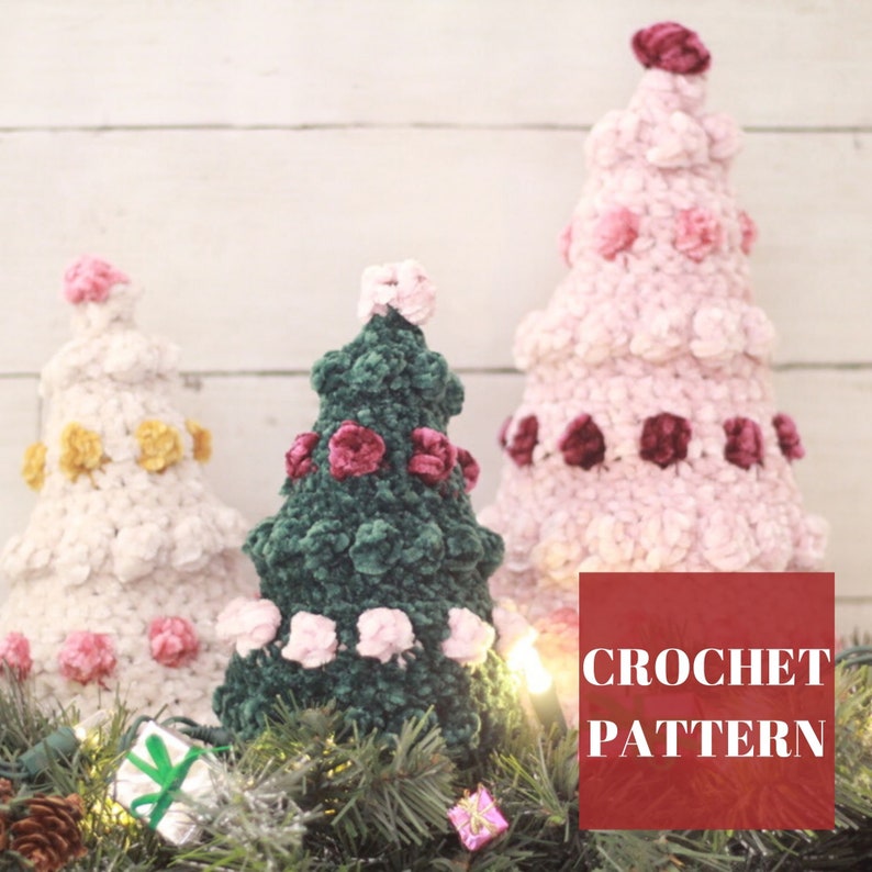 Puede incluir: Tres &aacute;rboles de Navidad tejidos a crochet en rosa, verde y blanco con hilo de terciopelo. Los &aacute;rboles est&aacute;n decorados con adornos de fieltro rosa y burdeos. Los &aacute;rboles est&aacute;n sentados en un lecho de ramas de pino con luces y peque&ntilde;os regalos. El texto "CROCHET PATTERN" est&aacute; en la esquina inferior derecha de la imagen.