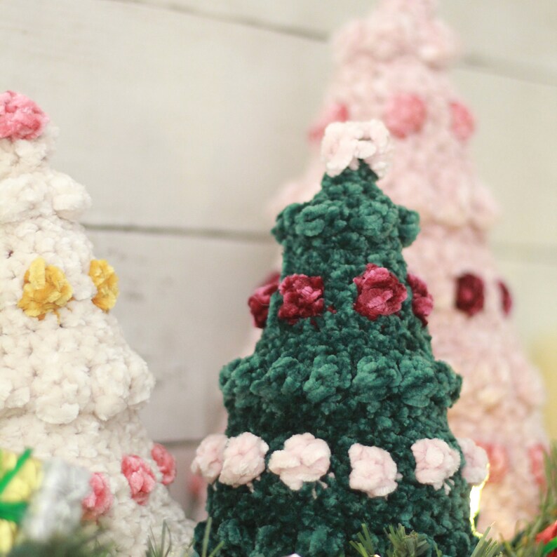 Puede incluir: Tres &aacute;rboles de Navidad de crochet, uno blanco con detalles amarillos y rosas, uno rosa con detalles rosas y uno verde con detalles rosas y burdeos.