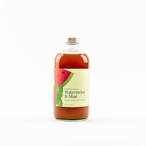 May include: A glass bottle of watermelon and mint flavored cocktail mixer from Wood Stove Kitchen. The bottle is clear and shows a red and green watermelon illustration on the label. The label also says "Watermelon & Mint" and "Natural Cocktail & Mocktail Mixer".