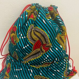 May include: A turquoise drawstring bag with a red and yellow floral pattern. The bag has a red drawstring and a small pocket on the front.