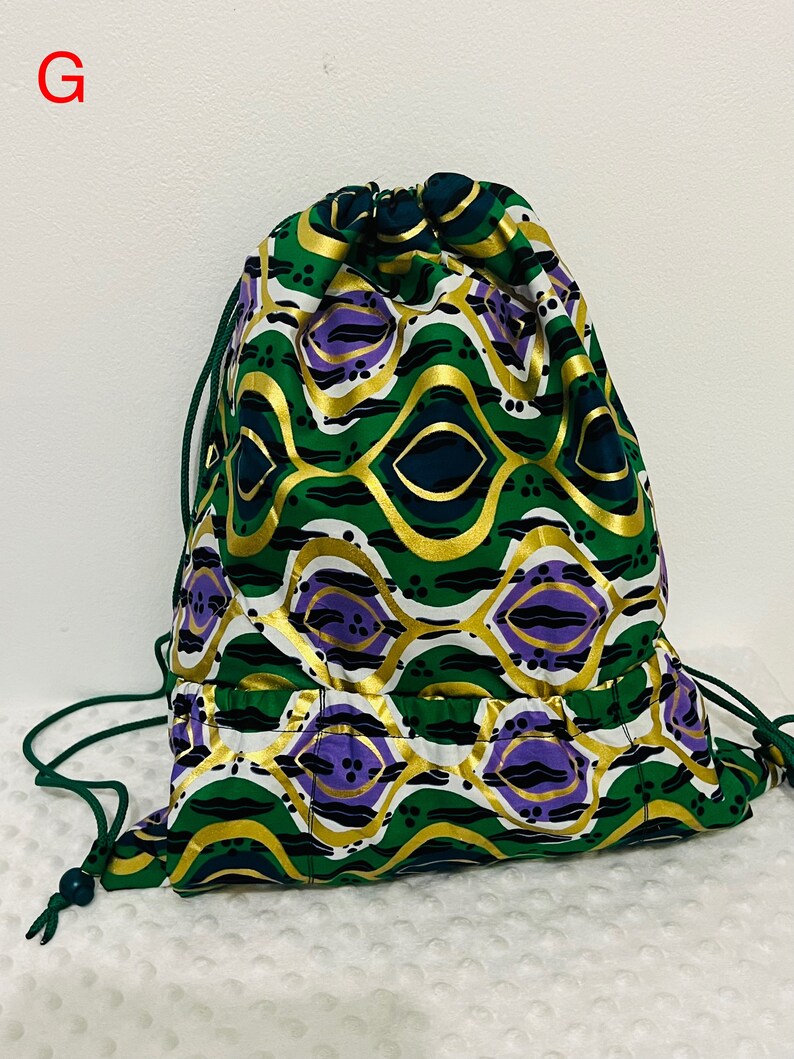 May include: A green, gold, and purple drawstring bag with a geometric pattern. The bag has a small pocket on the front.