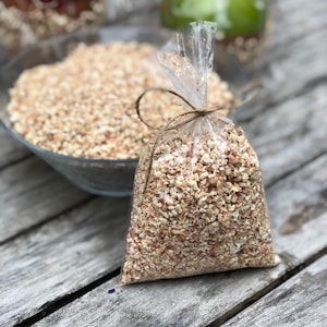 May include: A clear plastic bag filled with a mixture of white and brown dried corn kernels. The bag is tied with a brown twine string and is sitting on a wooden surface.