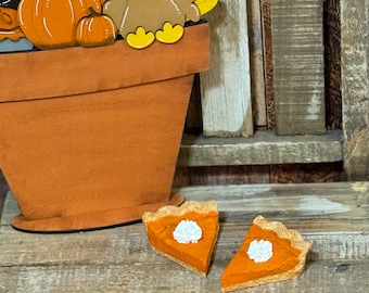 May include: Two miniature pumpkin pie slices with a dollop of whipped cream on top. The pies are on a rustic wooden surface.