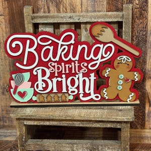 May include: A red and white wooden sign with the text "Baking Spirits Bright" and a gingerbread man, a rolling pin, and a mixing bowl.