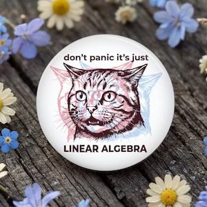 May include: A circular pinback button featuring a graphic of a cat with a startled expression. The design includes a red and blue color-shifted effect behind the cat. The text reads, "don't panic it's just LINEAR ALGEBRA" in dark brown lettering.