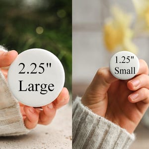 May include: Two white round buttons are displayed. One is labeled "2.25" Large" and the other is labeled "1.25" Small". The buttons are held in hands, with a blurred background of greenery and flowers.