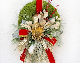 May include: A Christmas wreath featuring a moss base, decorated with red berries, gold and silver leaves, and a large red bow. A gold and red ribbon is used for hanging. A gold flower is at the centre.