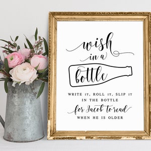 May include: A printable sign with a gold frame and white background. The sign says "wish in a bottle" with a drawing of a bottle. The text below says "Write it, roll it, slip it in the bottle for Jacob to read when he is older."