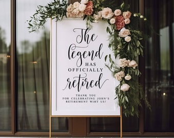 May include: A white sign with black calligraphy that reads "The legend has officially retired."  The sign is decorated with a floral garland of pink and white flowers and green leaves. The sign is on a gold stand.