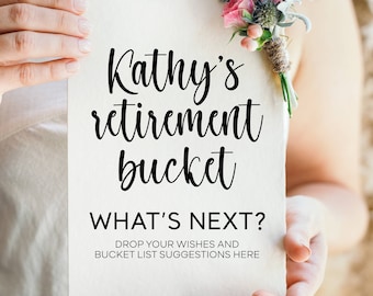 May include: A white card with black text that reads "Kathy's retirement bucket What's next? Drop your wishes and bucket list suggestions here". A woman is holding the card in front of her, and a bouquet of flowers is in the foreground.