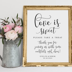 May include: A gold framed sign with the text "Love is Sweet" in black cursive font. The sign also includes the text "Please take a treat, thank you for joining us with some cocktails and cheer! EVELIN & DERIK 28.08.2025".
