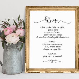 May include: A framed menu with a gold border, featuring a list of dishes including baby back ribs, pulled pork, and brisket. The menu is displayed on a white background with a floral arrangement in a metal pitcher.