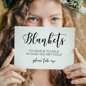 May include: A white sign with black calligraphy that reads "Blankets To Have & To Hold In Case You Get Cold Please Take One".