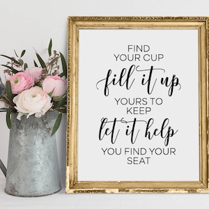 May include: A gold framed sign with the text "FIND YOUR CUP fill it up YOURS TO KEEP let it help YOU FIND YOUR SEAT" in black calligraphy.