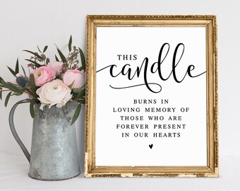 May include: A gold framed sign with the text "This candle burns in loving memory of those who are forever present in our hearts" with a small heart symbol at the bottom.
