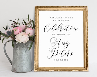 May include: A framed sign with gold trim reads "WELCOME TO THE RETIREMENT CELEBRATION IN HONOR OF Amy Peters 18.09.2021." A bouquet of pink and white flowers sits in a metal pitcher to the left of the sign.