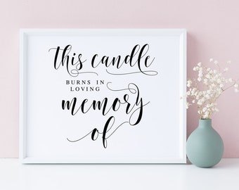 Puede incluir: Un cartel blanco enmarcado con caligrafía negra que dice "Esta vela arde en memoria cariñosa de". Un jarrón con flores blancas se encuentra sobre una superficie blanca.
