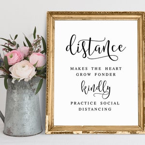 May include: A gold framed sign with the text "distance makes the heart grow fonder kindly practice social distancing" in black calligraphy font.