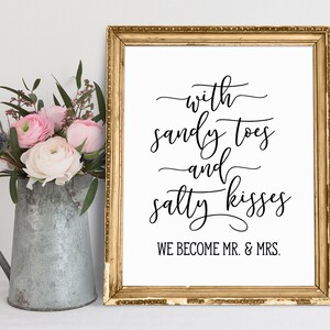 May include: A gold framed sign with white background and black calligraphy text that reads "with sandy toes and salty kisses we become mr. & mrs."