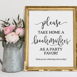 May include: A gold framed sign with white background and black text that reads "please take home a bookmark as a party favor! Thank you for celebrating with us today!"