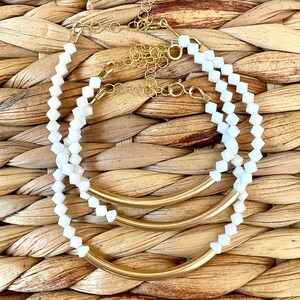 May include: Three gold metal hoops with white beads strung on them. The hoops are layered on top of each other and the beads are arranged in a symmetrical pattern.