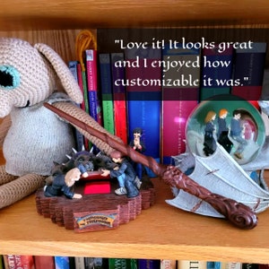 May include: A shelf displays a collection of Harry Potter memorabilia. Items include a wand, a snow globe with characters, and a figurine depicting a scene from the movie. Books with colorful spines and the text "Harry Potter" are visible.