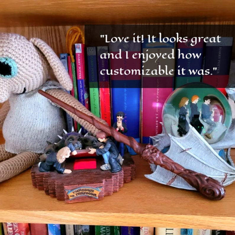 May include: A shelf displays a collection of Harry Potter memorabilia. Items include a wand, a snow globe with characters, and a figurine depicting a scene from the movie. Books with colorful spines and the text "Harry Potter" are visible.