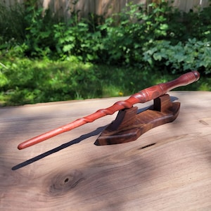 May include: A wooden wand with a reddish-brown finish, with a twisted design, resting on a wooden stand. The wand is approximately 13 inches long.