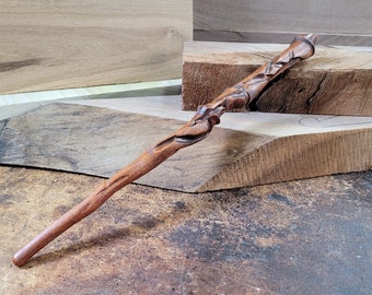 May include: A wooden wand with a unique, intricate design. The wand is carved with swirling patterns and has a natural brown color.