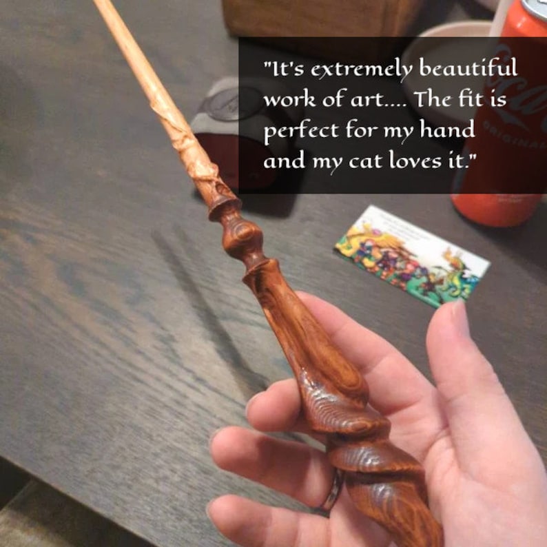May include: A handcrafted wooden wand with intricate carvings and a polished finish. The wand has a light-colored tip and a darker, detailed handle. The text on the image says, "It's extremely beautiful work of art... The fit is perfect for my hand and my cat loves it."