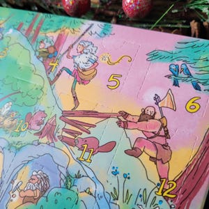 May include: A colorful cardboard advent calendar featuring a whimsical forest scene with illustrated characters, including a person with a spear, a bearded figure with an axe, and beavers. The calendar has numbered perforated doors from 4 to 12.