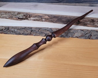 Peut inclure: Une baguette en bois brun foncé avec une pointe pointue et un bouton décoratif près de la poignée.