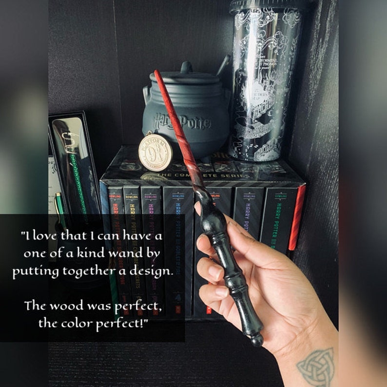 May include: A black and red wand with a twisted handle. The wand is held in a person's hand. The image includes a black cauldron, a Harry Potter themed cup, and a series of Harry Potter books.