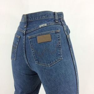 May include: A pair of blue denim jeans with a brown leather patch on the back pocket that says "Wrangler".