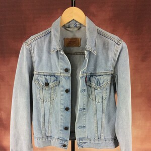 May include: A light blue denim jacket with a button closure, two chest pockets, and two front pockets. The jacket has a classic design and is made of a soft, comfortable material.