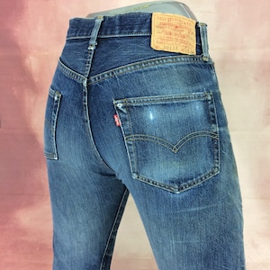 May include: A pair of blue denim jeans with a brown leather patch on the back pocket that reads "Levi Strauss & Co. Quality Clothing XX. Every Garment Guaranteed 501XX", and a red tab with the word "Levi's" on the back right pocket.