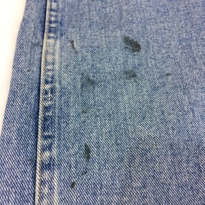 May include: Close-up of blue denim fabric with several dark blue stains.