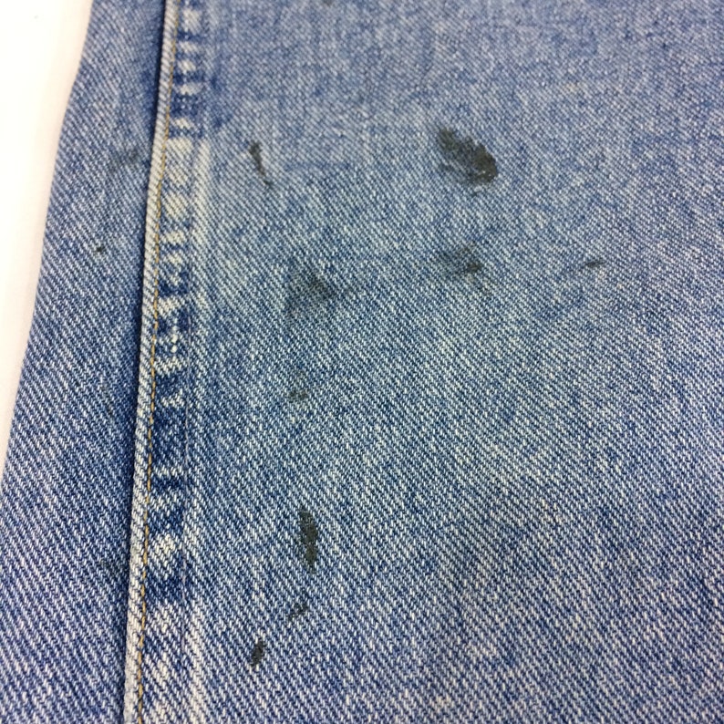 May include: Close-up of blue denim fabric with several dark blue stains.