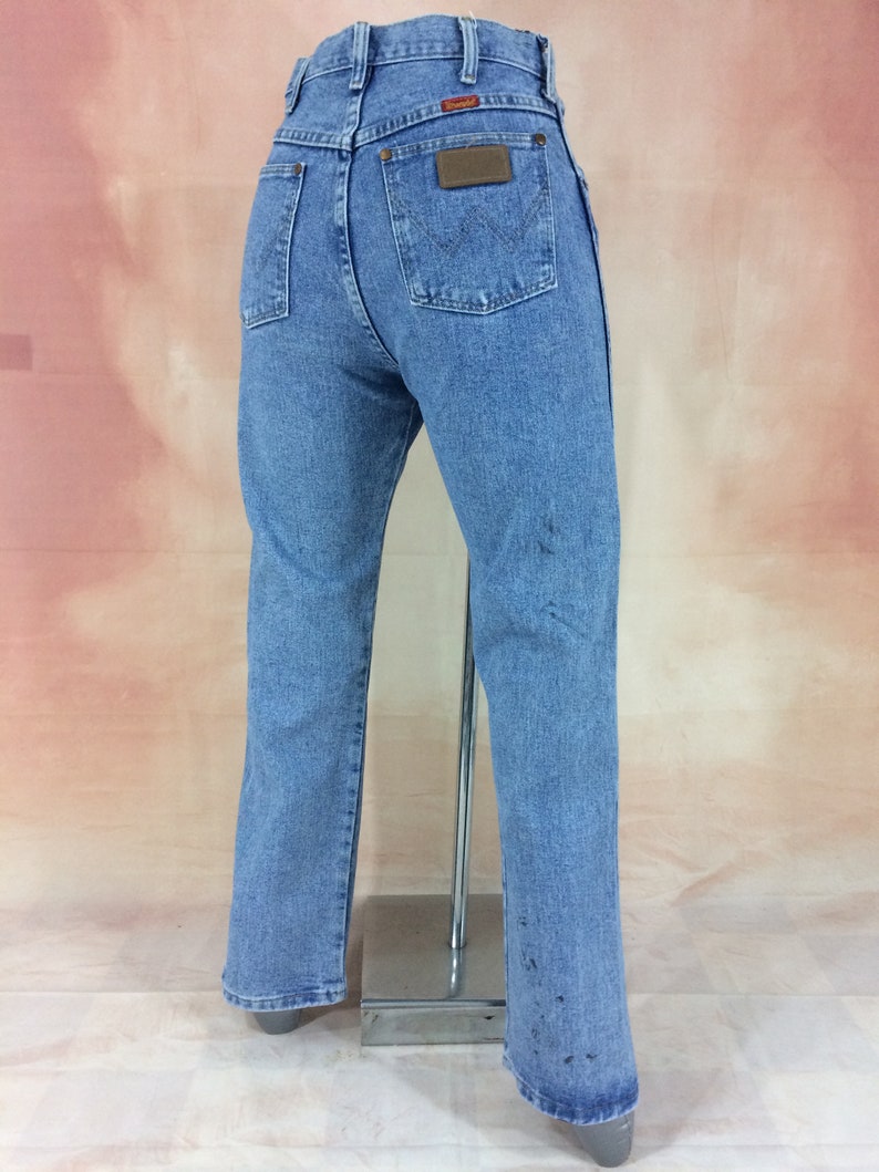May include: A pair of light blue denim jeans with a brown leather patch on the back pocket that says "Wrangler".