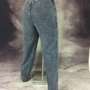 May include: Acid wash denim jeans with a high waist and cuffed hems. The jeans have a classic five-pocket design and a button and zipper closure. The denim has a faded, textured appearance.