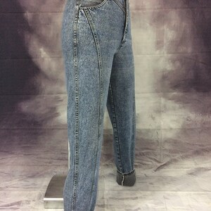May include: Light blue denim jeans with a high waist and a tapered leg. The jeans feature a unique seam design on the front and back, with cuffed hems. The denim has a faded, acid-wash appearance, and the jeans are displayed on a mannequin.